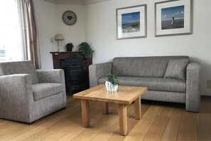 Ein Wohnzimmer mit grauem Sofa, zwei Sesseln, einem Holztisch und einem Kamin.