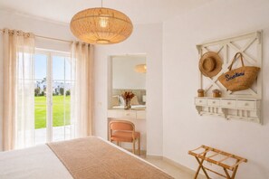 Ein Schlafzimmer mit einem großen Bett, einem Holzstuhl, einer Korbschaukel-Lampe, einem Spiegel und einem an der Wand befestigten Regal mit Hüten und einer Tasche.