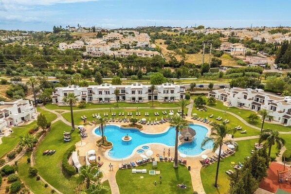 Un resort con piscina central, varias edificaciones y un área ajardinada.