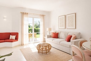 Ein modernes Wohnzimmer mit einem roten Sofa, einem beige farbenen Sofa mit roten Kissen, einem Korpus-Couchtisch und einem Glastisch mit Stühlen.