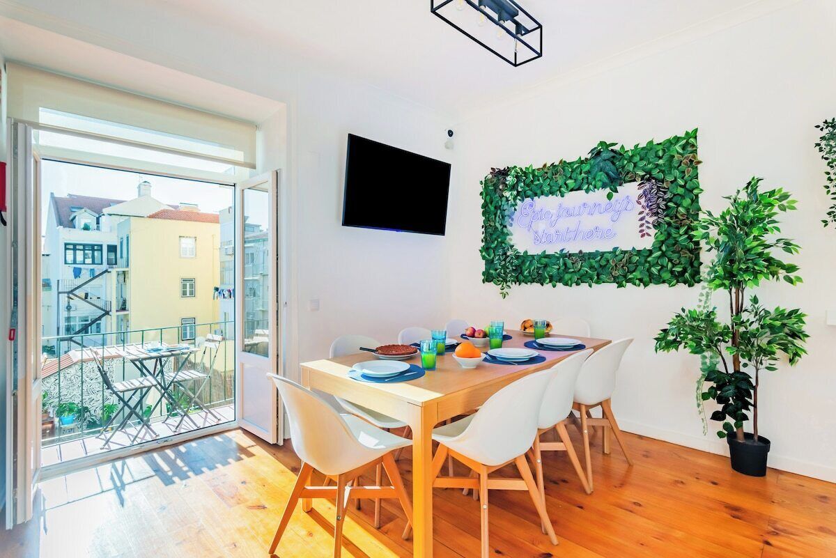 Un coin repas avec une table dressée pour quatre personnes, une plante en pot et un téléviseur fixé au mur.
