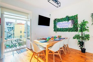 A dining area with a table set for four, a potted plant, and a wall-mounted TV. - Double Room @ Guest Inn 1 Boutique House (campo pequeno)
