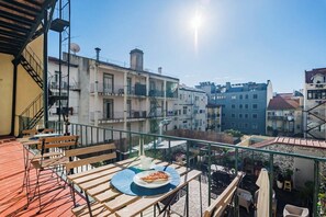 A balcony with wooden furniture, a pizza on a plate, and a view of surrounding buildings. - Double Room @ Guest Inn 1 Boutique House (campo pequeno)