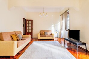 A living room with a sofa, a smaller couch, a TV on a stand, a rug, and a door. - Marquês de Pombal Classical Living (Lisbon)