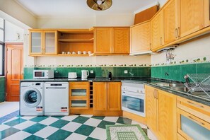 A compact kitchen with wooden cabinets, a washing machine, an oven, and a microwave. - Marquês de Pombal Classical Living (Lisbon)