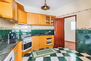 A kitchen with wooden cabinets, a stove, a sink, and a green and white checkered floor. - Marquês de Pombal Classical Living (Lisbon)