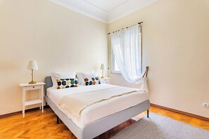 A bedroom with a bed, bedside tables, a window with sheer curtains, and a wooden floor. - Marquês de Pombal Classical Living (Lisbon)