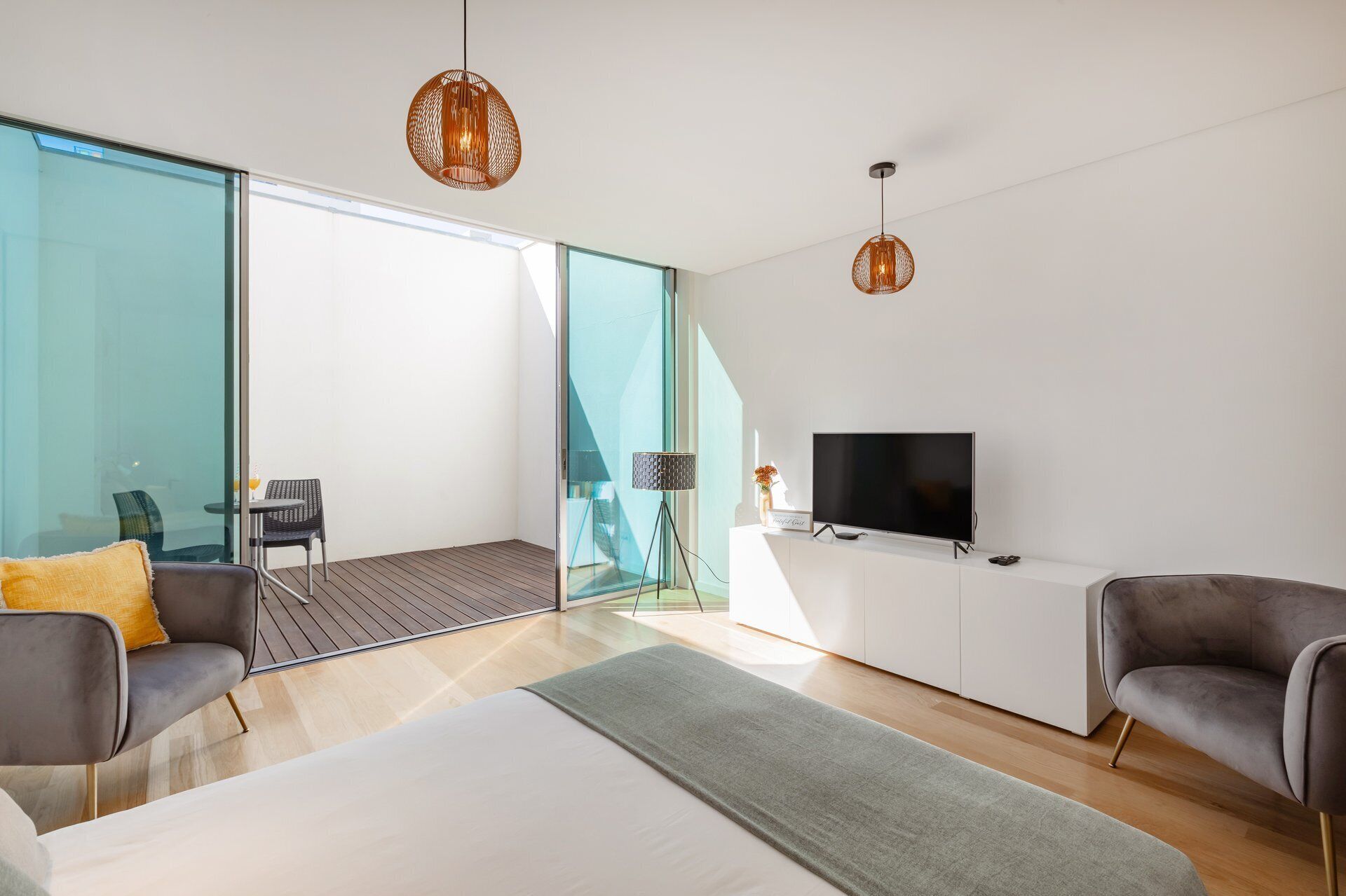 Ein modernes Schlafzimmer mit einem Bett, zwei Sesseln, einem Fernseher und einem Balkon mit Glastür.