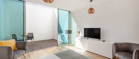 Et moderne soveværelse med seng, to lænestole, et fjernsyn og en balkon med glasdør.