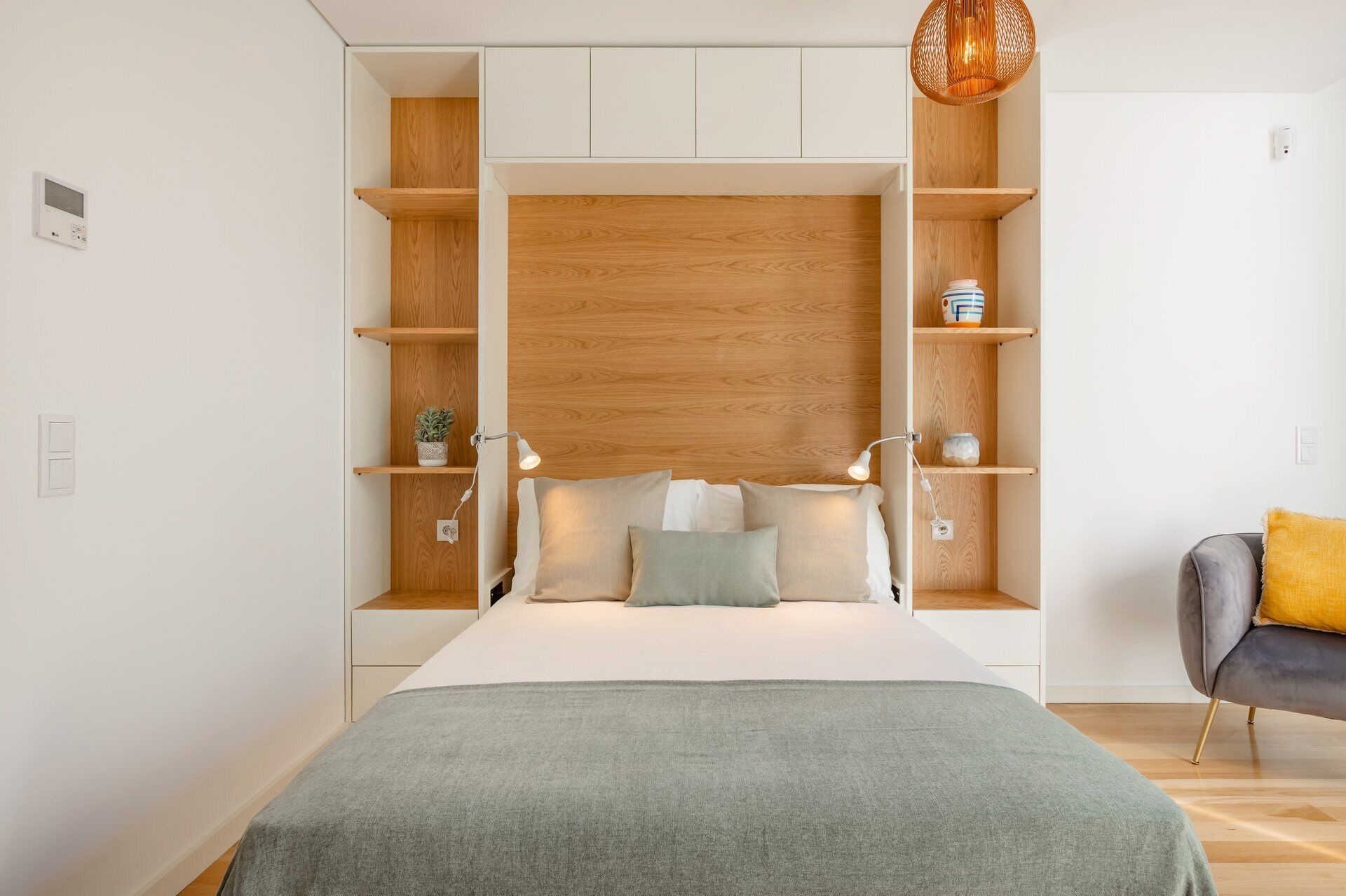Un dormitorio moderno con cama, estanterías empotradas, lámparas de noche y una lámpara colgante.