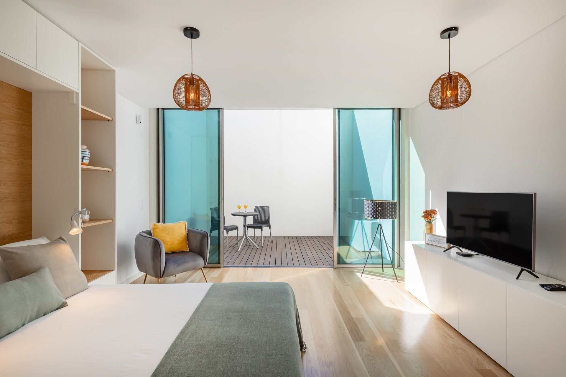 Quarto de hotel moderno com cama, televisão, sofá, mesinha com duas cadeiras e varanda com vista.
