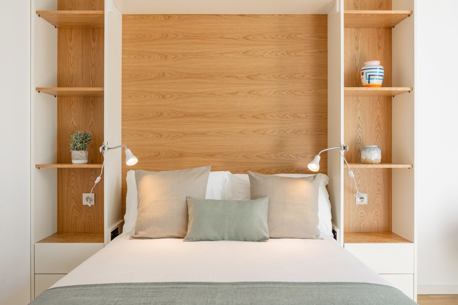 A bedroom with a bed, two bedside tables, a nightstand, and a wooden headboard.