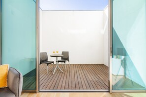 A balcony with a wooden floor, two wicker chairs, a small round table, and two glasses of orange juice. - Stylish Studio @ Matosinhos (Matosinhos)