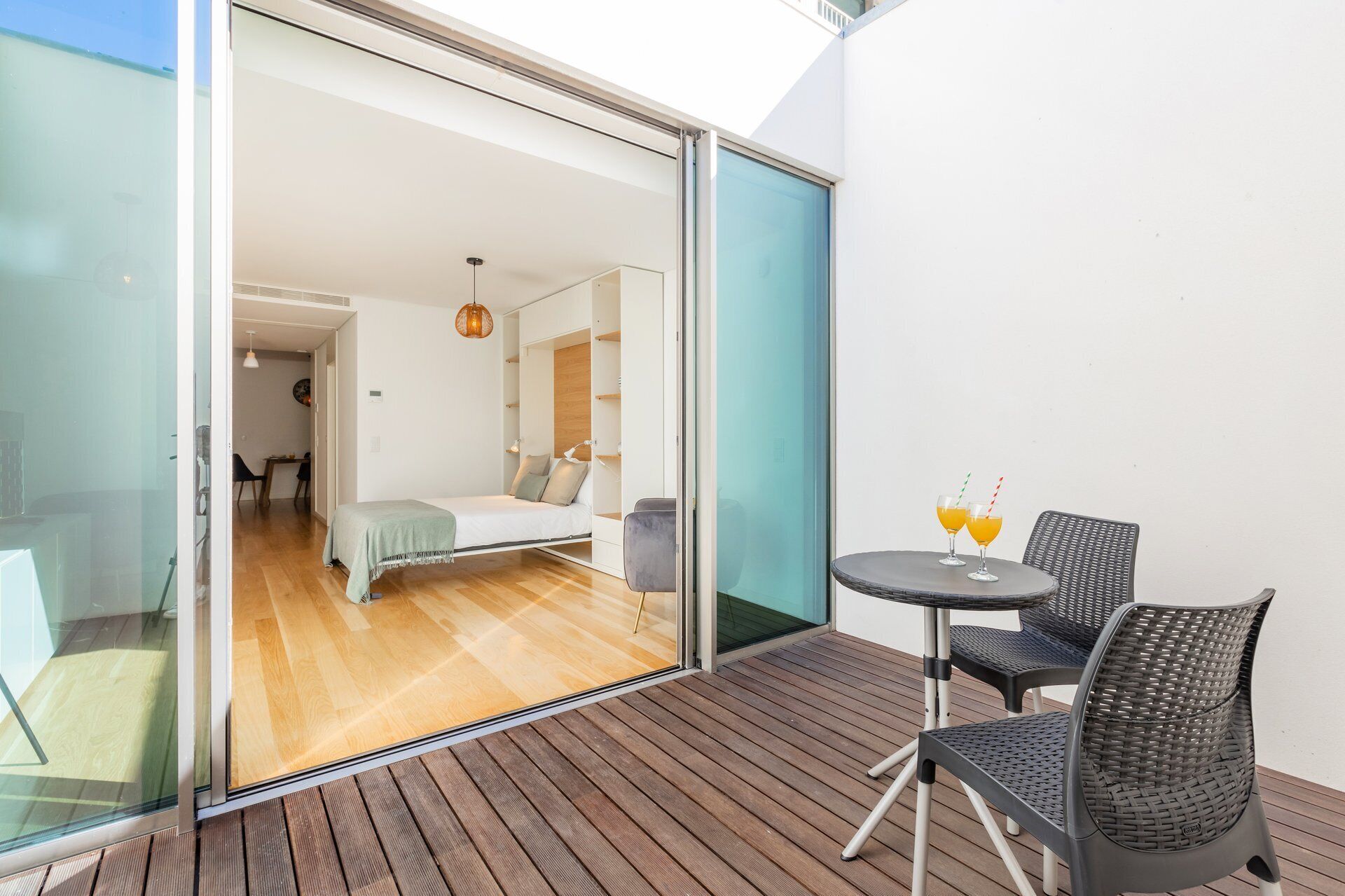 Ein modernes Zimmer mit einem Bett, einem kleinen Tisch mit Stühlen und einer Glastür zu einem Außenbereich mit einer Holzterrasse.