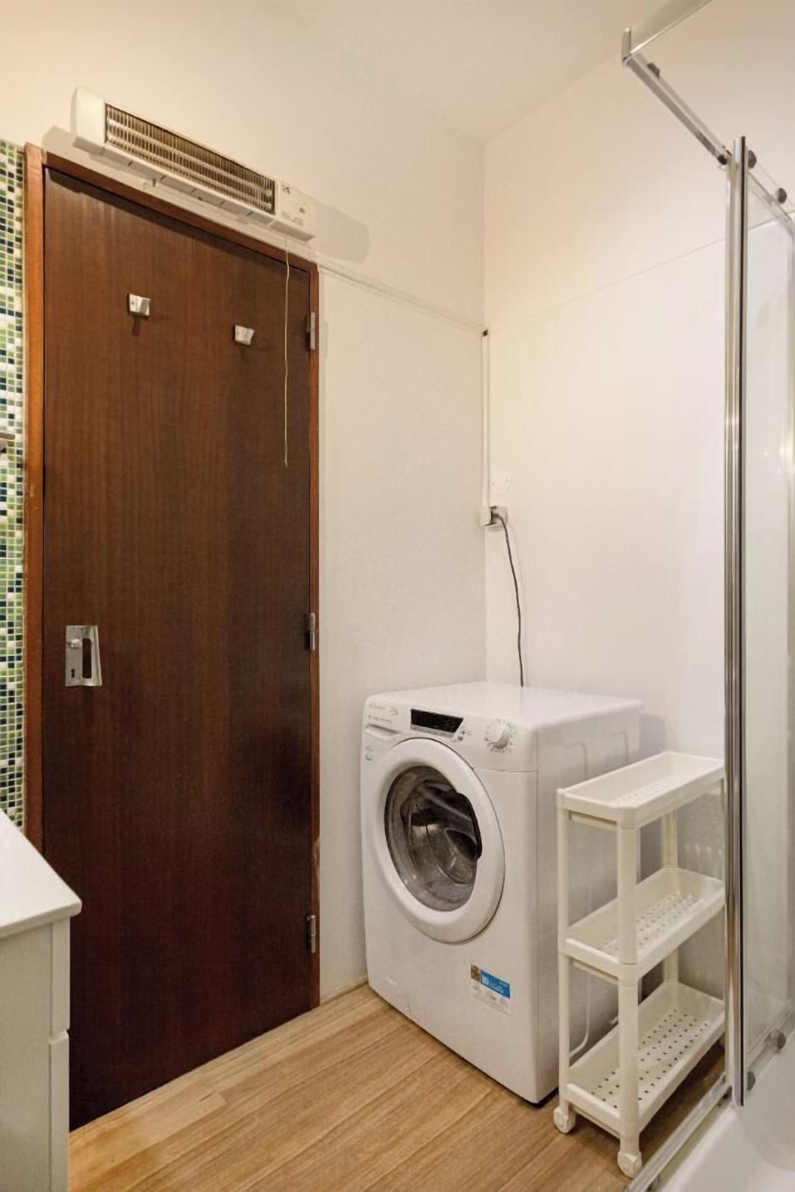 A compact laundry room with a washing machine, a drying rack, and a glass shower enclosure.