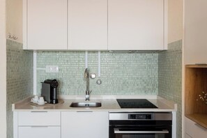 A kitchen with white cabinets, a sink, a coffee maker, and a built-in oven. - Sky View Studio em Cascais (Cascais)