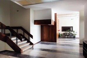 A hotel lobby with a staircase, a wooden door, a flat-screen TV, and potted plants. - Sky View Studio em Cascais (Cascais)