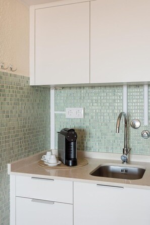 A kitchen with a coffee maker, a sink, and a tiled backsplash. - Sky View Studio em Cascais (Cascais)