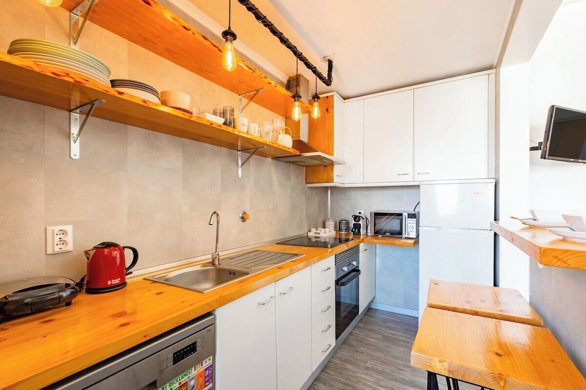 A modern kitchen with wooden shelves, a sink, a microwave, and a red kettle.