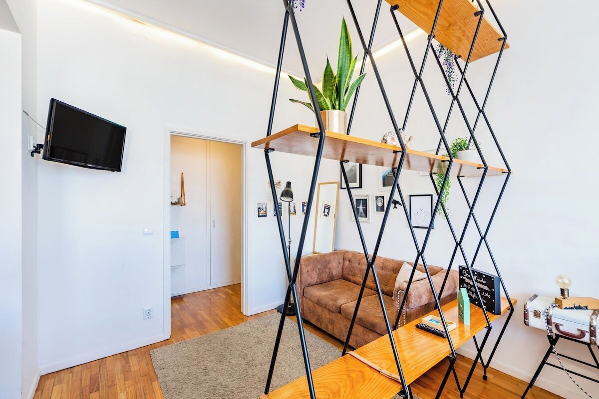 Un soggiorno moderno con divano, tavolino in legno, televisione a parete e una libreria geometrica con piante.