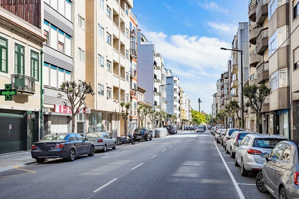 Une rue bordée d’immeubles résidentiels à plusieurs étages, de voitures garées et sous un ciel dégagé.