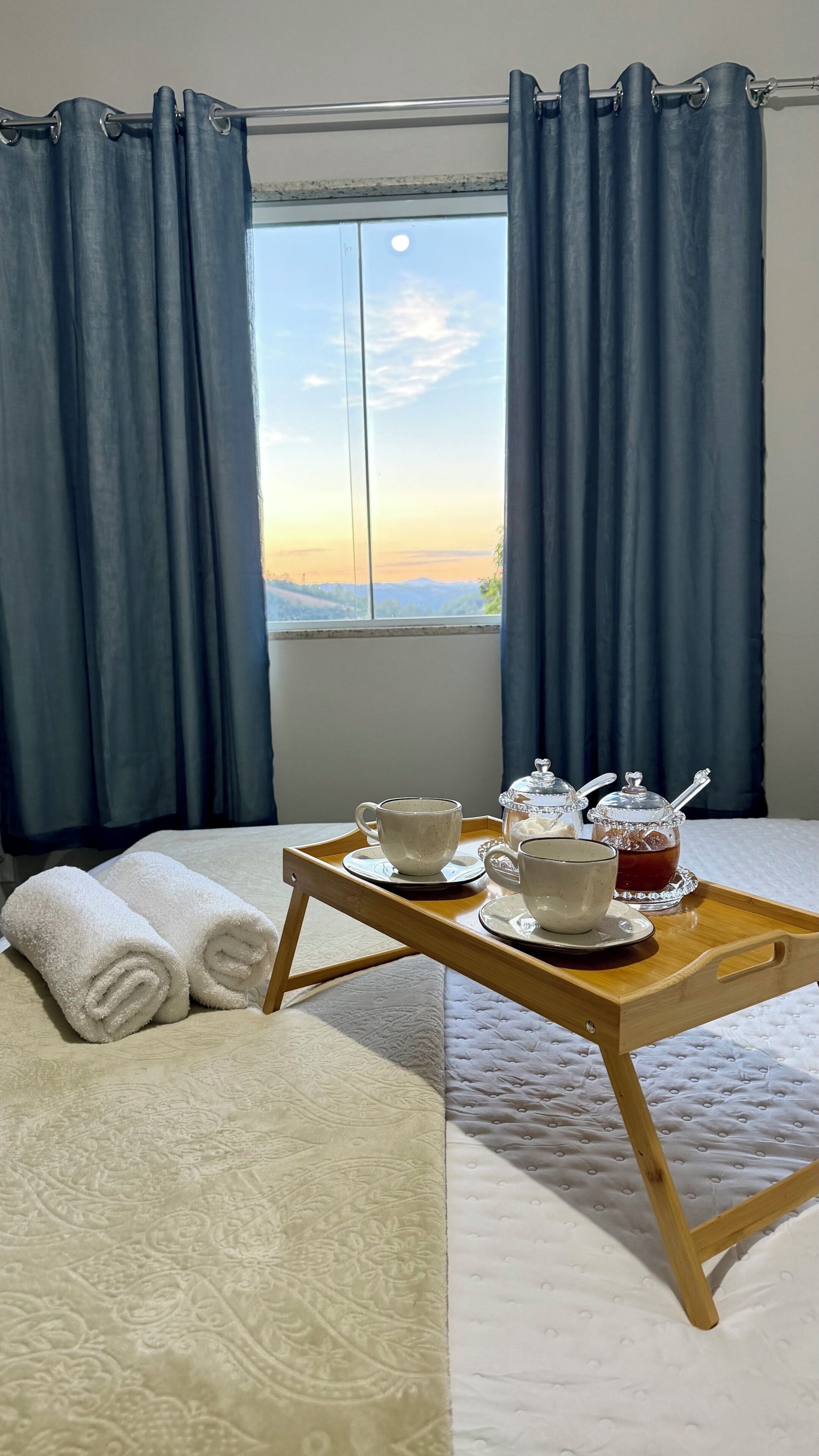 Une chambre d’hôtel avec un lit, un plateau avec du thé et de la crème, et une vue sur les montagnes par la fenêtre.