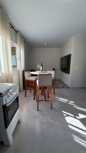 Una cocina moderna con horno empotrado, comedor con sillas, una mesa y un televisor montado en la pared.