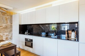 A modern kitchen with white cabinets, a black countertop, and a stone wall. - Porto Loft Living (Porto)