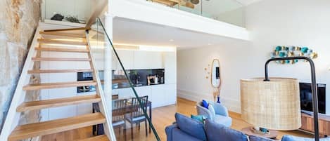 A modern interior with a wooden staircase, a dining area, and a living room with a sofa and a lamp.