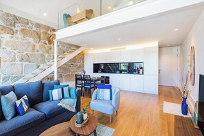 A modern interior with a stone wall, a staircase, a living area with a sofa and chairs, a kitchen area, and a dining table. - Porto Loft Living (Porto)