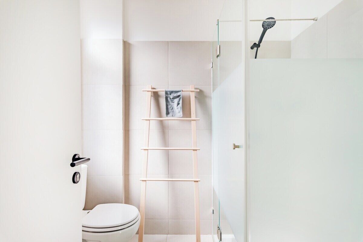 A bathroom with a toilet, a shower, and a wooden shelf.