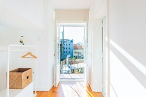 A narrow hallway with a wooden floor, a white door, and a view of buildings through an open door. - Superior Suite @ Guest Inn 2 Boutique House (campo pequeno)