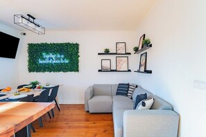 A modern living room with a dining area, a grey sofa, and a neon sign on the wall. - Superior Suite @ Guest Inn 2 Boutique House (campo pequeno)