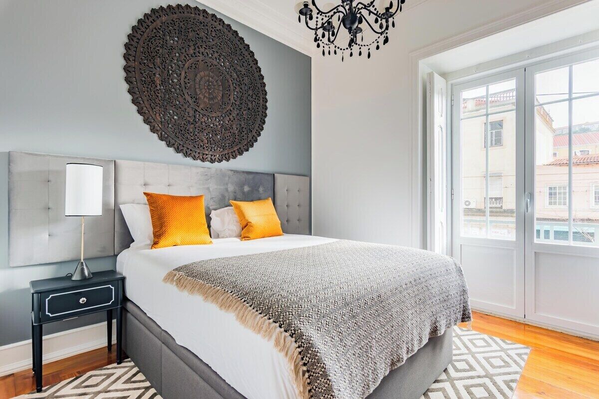 A bedroom with a large bed, a decorative wall piece, a nightstand, and a view through a window.