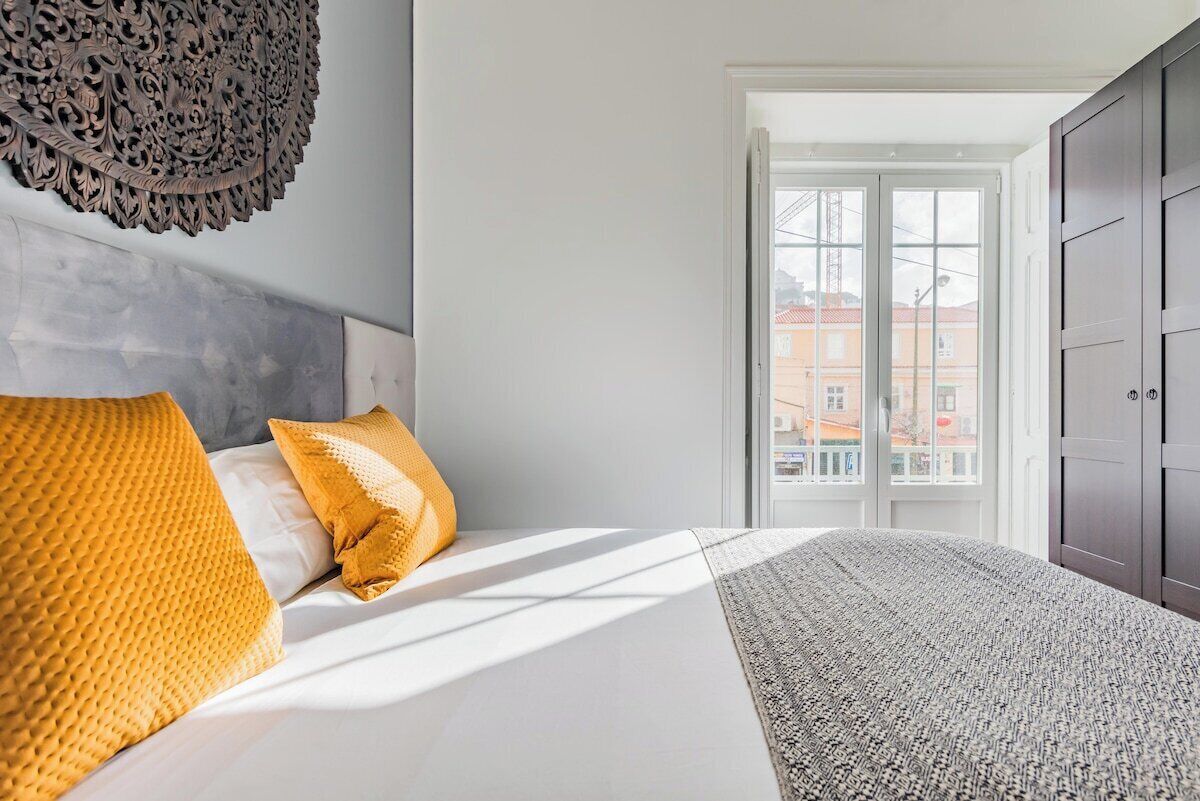 Une chambre à coucher avec un lit, deux oreillers, un tapis à motifs, une décoration murale et une vue à travers une porte.