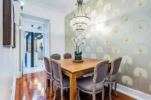 A dining area with a wooden table, chairs, a chandelier, and a wall with a dandelion pattern. - Stylish 2BR Apartment | Ideal for Monthly Stays (Lisbon)