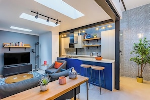 A modern living space with a kitchen, dining area, and a TV in a compact apartment. - Stylish 2BR Apartment | Ideal for Monthly Stays (Lisbon)