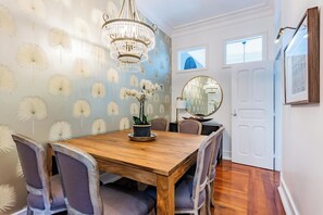 Un comedor con una mesa de madera, sillas, una lámpara de araña y una pared decorada con motivos de diente de león.