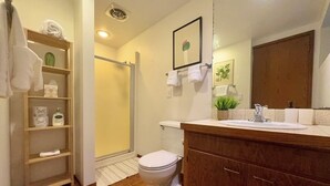 Une salle de bain comprenant des toilettes, un lavabo, un meuble-lavabo en bois et un espace douche.
