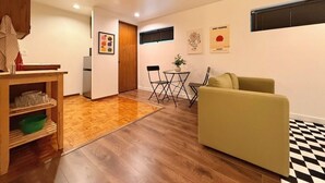 Un salon avec un canapé, une petite table et un fauteuil. On y trouve également un meuble en bois et un tapis sur le sol.