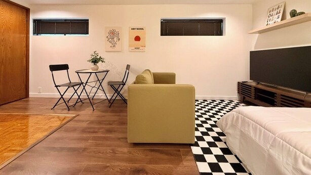Une pièce de taille modeste comprenant un lit, un canapé, une table à manger avec des chaises, une petite plante en pot et des œuvres d’art accrochées aux murs.