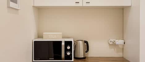 A kitchen with a microwave, a kettle, and a power outlet on a wooden countertop.