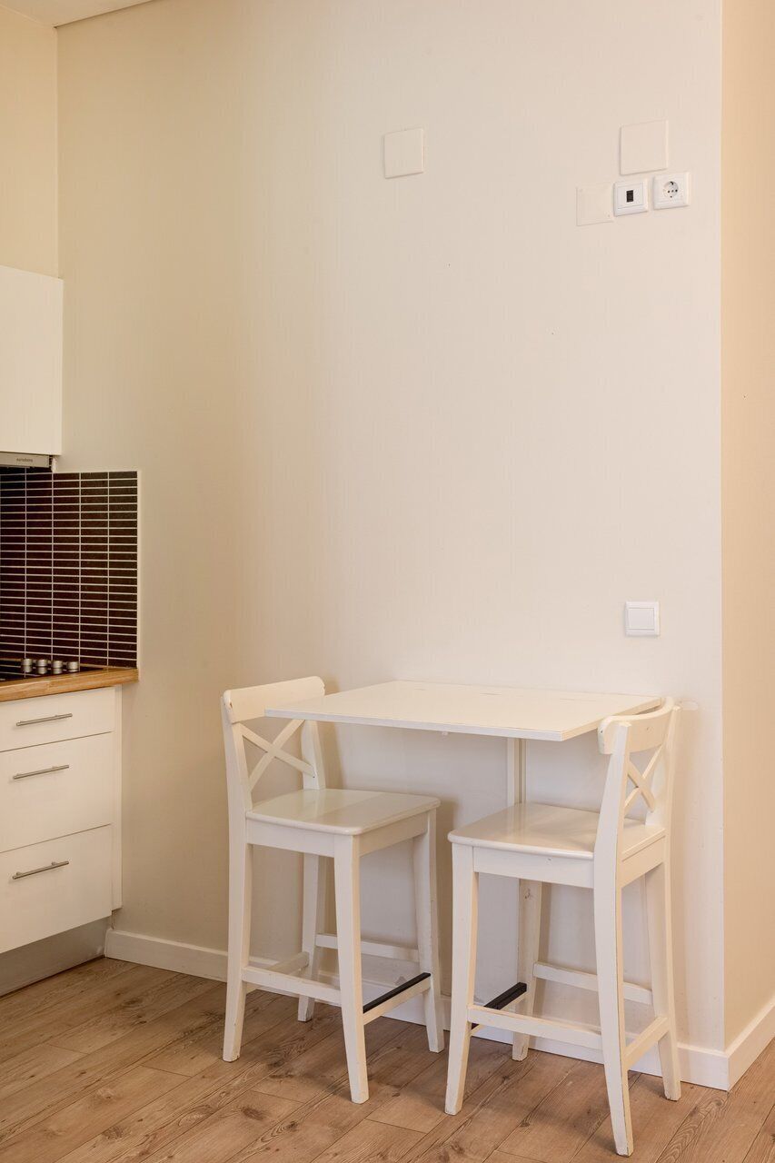 Una habitación con un escritorio blanco y dos sillas blancas, un armario de madera y un salpicadero de azulejos.