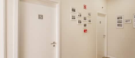 A hallway with doors marked with 'S', a fire alarm, and framed pictures on the wall.