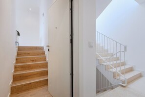 Una escalera de madera que conduce a una puerta blanca, y otra escalera con escalones blancos y barandillas de metal.