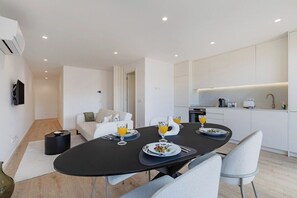 Un comedor moderno y minimalista con una mesa negra dispuesta para dos personas, sillas blancas y una cocina al fondo.