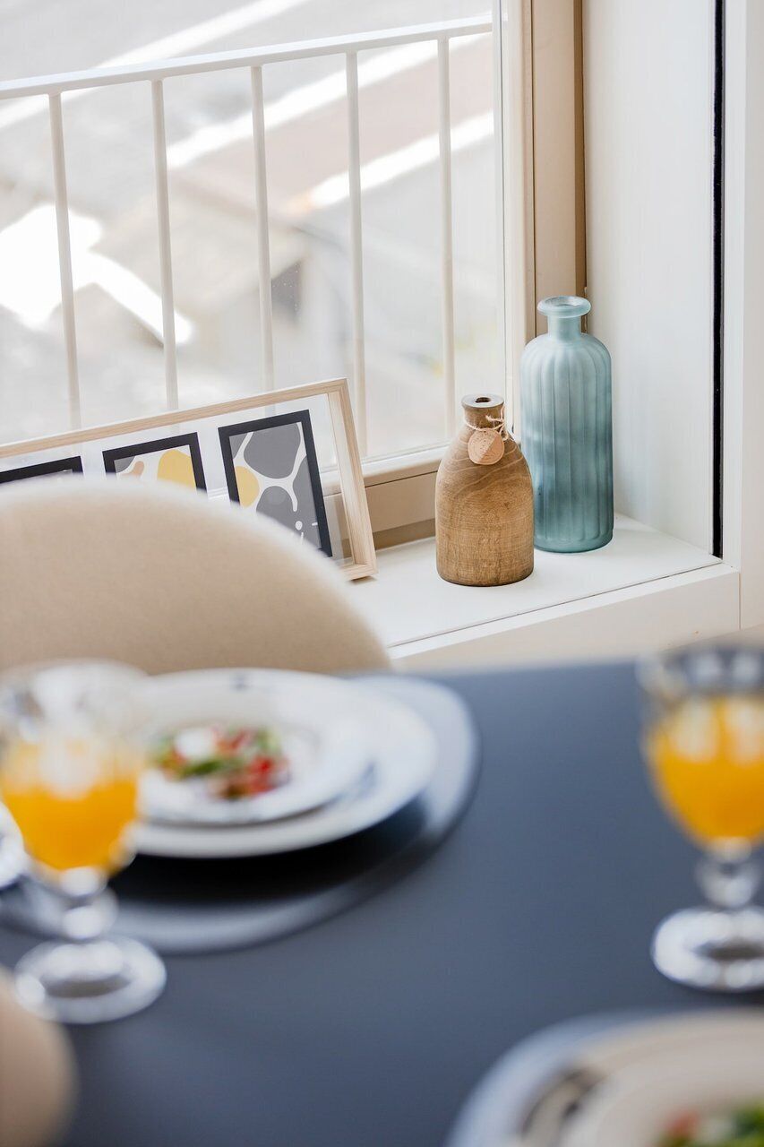 Un coin repas avec une table dressée pour deux personnes, une fenêtre offrant une belle vue et des vases décoratifs posés sur le rebord de la fenêtre.