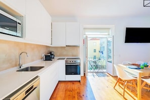 A modern kitchen with white cabinets, a built-in oven, and a sink. There is a dining area with a table and chairs, and a view of the outside. - Pop Art Double Room @ Guest Inn 1 Boutique House (campo pequeno)