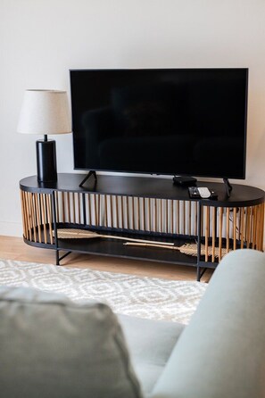 Una sala de estar moderna con un televisor de pantalla plana sobre una consola negra, una lámpara y un tapete estampado.