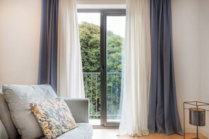 A room with a sofa, a window with curtains, and a view of greenery outside. - Paraíso Porto Living (Porto)